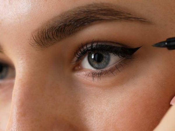 Close-up of a woman applying kohl eyeliner with an applicator stick for precise lash line definition.