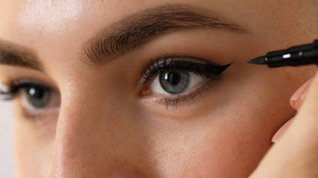 Close-up of a woman applying kohl eyeliner with an applicator stick for precise lash line definition.