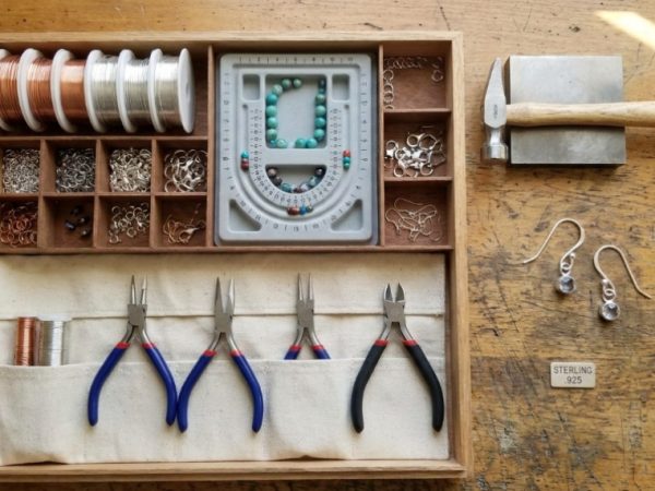 Flat lay of jewelry kit and silver earring hooks on wooden table.