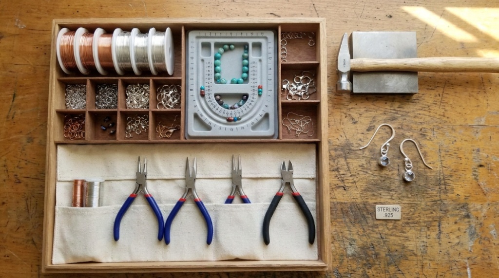 Flat lay of jewelry kit and silver earring hooks on wooden table.